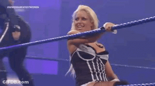 A Woman Is Standing In A Wrestling Ring Holding A Rope And Smiling . GIF