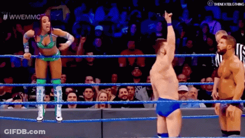 A Woman Is Standing In A Wrestling Ring With A Referee And A Man Standing Behind Her . GIF