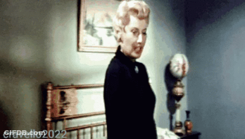 A Woman Is Standing In Front Of A Bed In A Room With The Year 2022 On The Bottom Right GIF