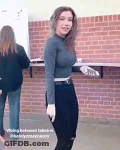 A Woman Is Standing In Front Of A Brick Wall And Holding A Bottle Of Water . GIF