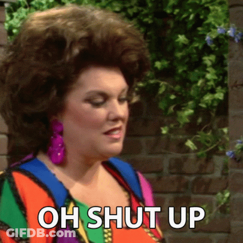 A Woman Is Standing In Front Of A Brick Wall And Says " Oh Shut Up " GIF