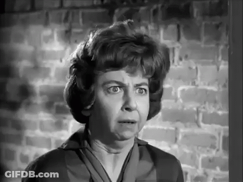 A Woman Is Standing In Front Of A Brick Wall Making A Funny Face . GIF