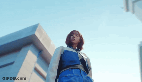 A Woman Is Standing In Front Of A Building And Looking Down At The Camera . GIF