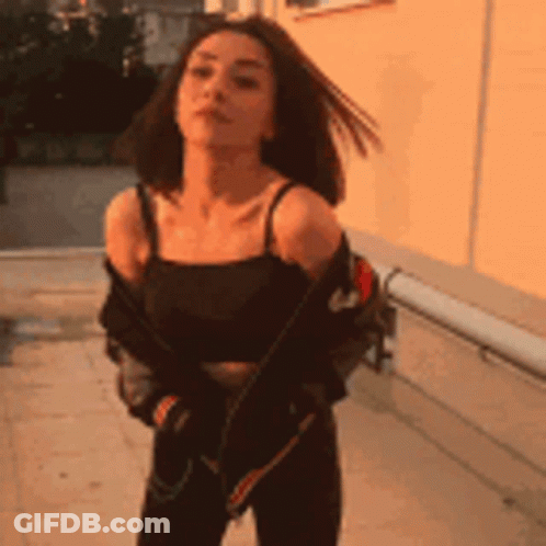 A Woman Is Standing In Front Of A Building Wearing A Black Tank Top And A Jacket . GIF