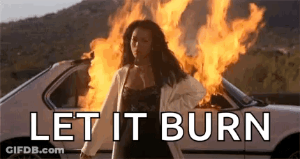 A Woman Is Standing In Front Of A Car On Fire . GIF