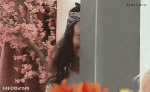 A Woman Is Standing In Front Of A Cherry Blossom Tree And Looking Out Of A Window . GIF