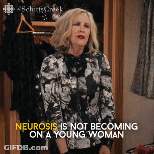 A Woman Is Standing In Front Of A Closet With The Words " Neurosis Is Not Becoming On A Young Woman " Written Below Her GIF