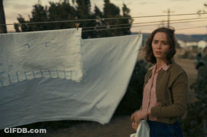 A Woman Is Standing In Front Of A Clothesline With A White Cloth Hanging On It GIF