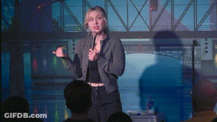 A Woman Is Standing In Front Of A Crowd Holding A Microphone And Giving A Speech . GIF
