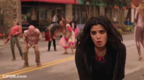 A Woman Is Standing In Front Of A Crowd Of Zombies . GIF