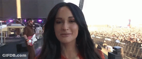 A Woman Is Standing In Front Of A Crowd While A Man Plays A Guitar GIF