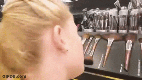 A Woman Is Standing In Front Of A Display Of Makeup Brushes GIF