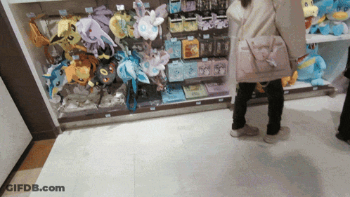 A Woman Is Standing In Front Of A Display Of Stuffed Animals Including One That Says Eevee GIF