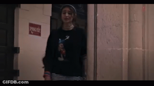 A Woman Is Standing In Front Of A Door In A Dark Room . GIF