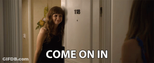 A Woman Is Standing In Front Of A Door That Says 118 And Says Come On In GIF