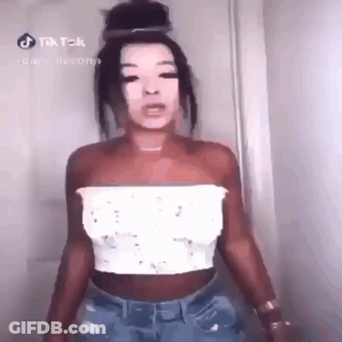 A Woman Is Standing In Front Of A Door Wearing A White Top And Blue Jeans . GIF