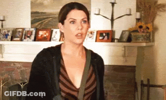 A Woman Is Standing In Front Of A Fireplace In A Living Room With Pictures On The Wall . GIF