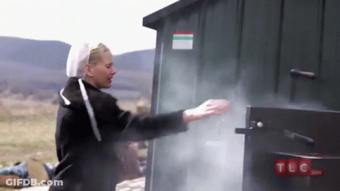 A Woman Is Standing In Front Of A Green Shed With Smoke Coming Out Of It .. GIF