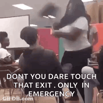 A Woman Is Standing In Front Of A Group Of People In A Classroom While A Man Sits In A Chair . GIF