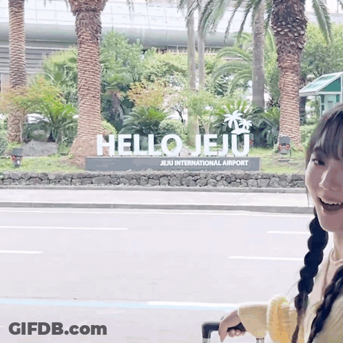 A Woman Is Standing In Front Of A Hello Jeju Sign GIF