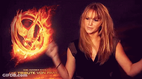 A Woman Is Standing In Front Of A Hunger Games Poster GIF