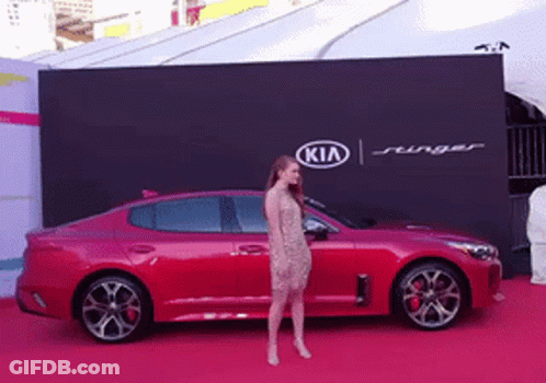 A Woman Is Standing In Front Of A Kia Advertisement GIF