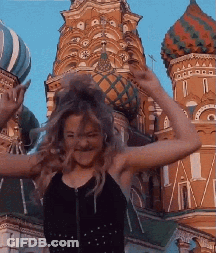 A Woman Is Standing In Front Of A Large Building With Her Hair In The Air . GIF