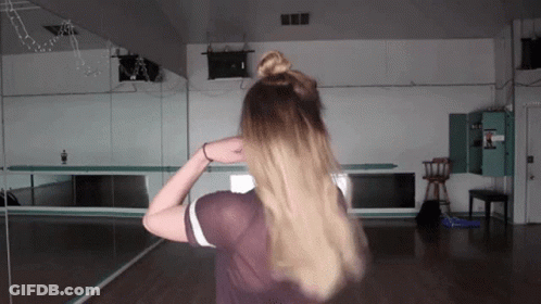 A Woman Is Standing In Front Of A Large Mirror GIF
