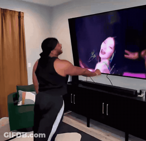 A Woman Is Standing In Front Of A Large Television Screen GIF