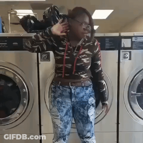 A Woman Is Standing In Front Of A Laundromat Machine With A Sign That Says Warning GIF