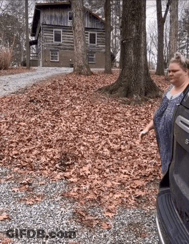 A Woman Is Standing In Front Of A Log Cabin In The Woods GIF