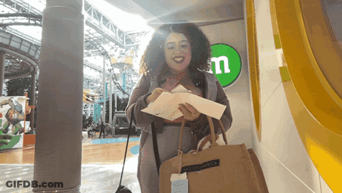 A Woman Is Standing In Front Of A M & M Sign GIF