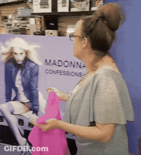 A Woman Is Standing In Front Of A Madonna Confessions Sign GIF