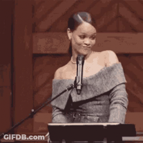 A Woman Is Standing In Front Of A Microphone And A Piano . GIF