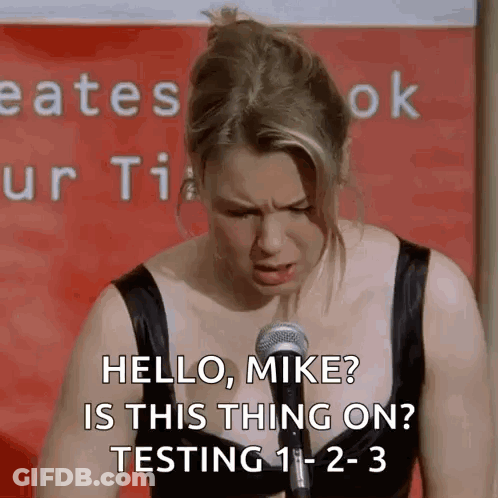 A Woman Is Standing In Front Of A Microphone And Saying Hello , Mike ? Is This Thing On ? Testing 1-2-3 GIF