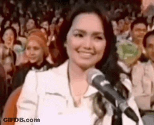 A Woman Is Standing In Front Of A Microphone And Smiling . GIF