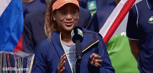 A Woman Is Standing In Front Of A Microphone And Smiling While Wearing An Orange Hat . GIF