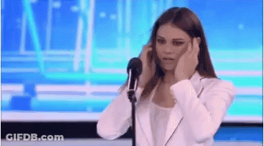 A Woman Is Standing In Front Of A Microphone Covering Her Ears . GIF