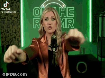 A Woman Is Standing In Front Of A Microphone With Her Arms Outstretched GIF