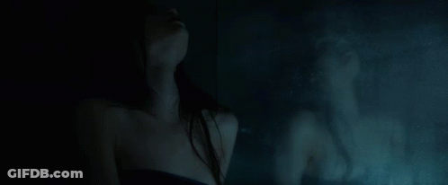 A Woman Is Standing In Front Of A Mirror In A Dark Room With Her Reflection In The Mirror . GIF