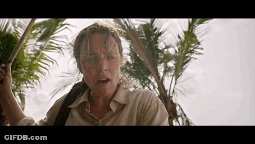 A Woman Is Standing In Front Of A Palm Tree Holding A Stick GIF