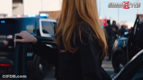 A Woman Is Standing In Front Of A Police Car With The Words Snake Eyes Behind Her GIF