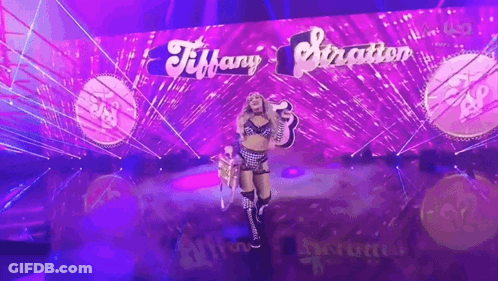 A Woman Is Standing In Front Of A Purple Wall That Says Tiffany Stratton GIF