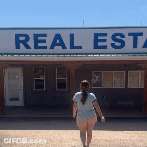A Woman Is Standing In Front Of A Real Estate Sign GIF