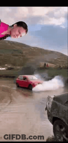 A Woman Is Standing In Front Of A Red Car That Is Drifting In The Water . GIF