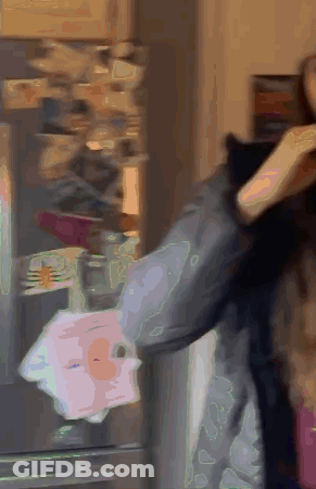 A Woman Is Standing In Front Of A Refrigerator Holding A Piece Of Paper GIF