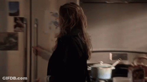 A Woman Is Standing In Front Of A Refrigerator In A Kitchen . GIF