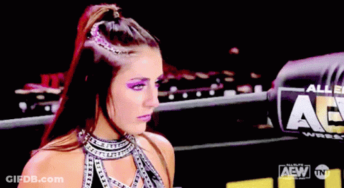 A Woman Is Standing In Front Of A Sign That Says Aew On It GIF