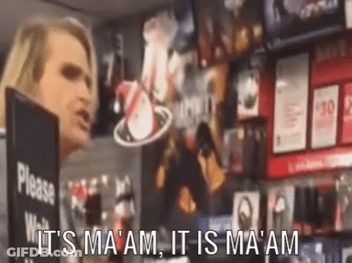 A Woman Is Standing In Front Of A Sign That Says Please Wait It 'S Ma 'Am It Is Ma 'Am GIF