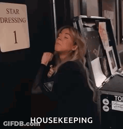 A Woman Is Standing In Front Of A Sign That Says Star Dressing 1 And A Box That Says Housekeeping . GIF